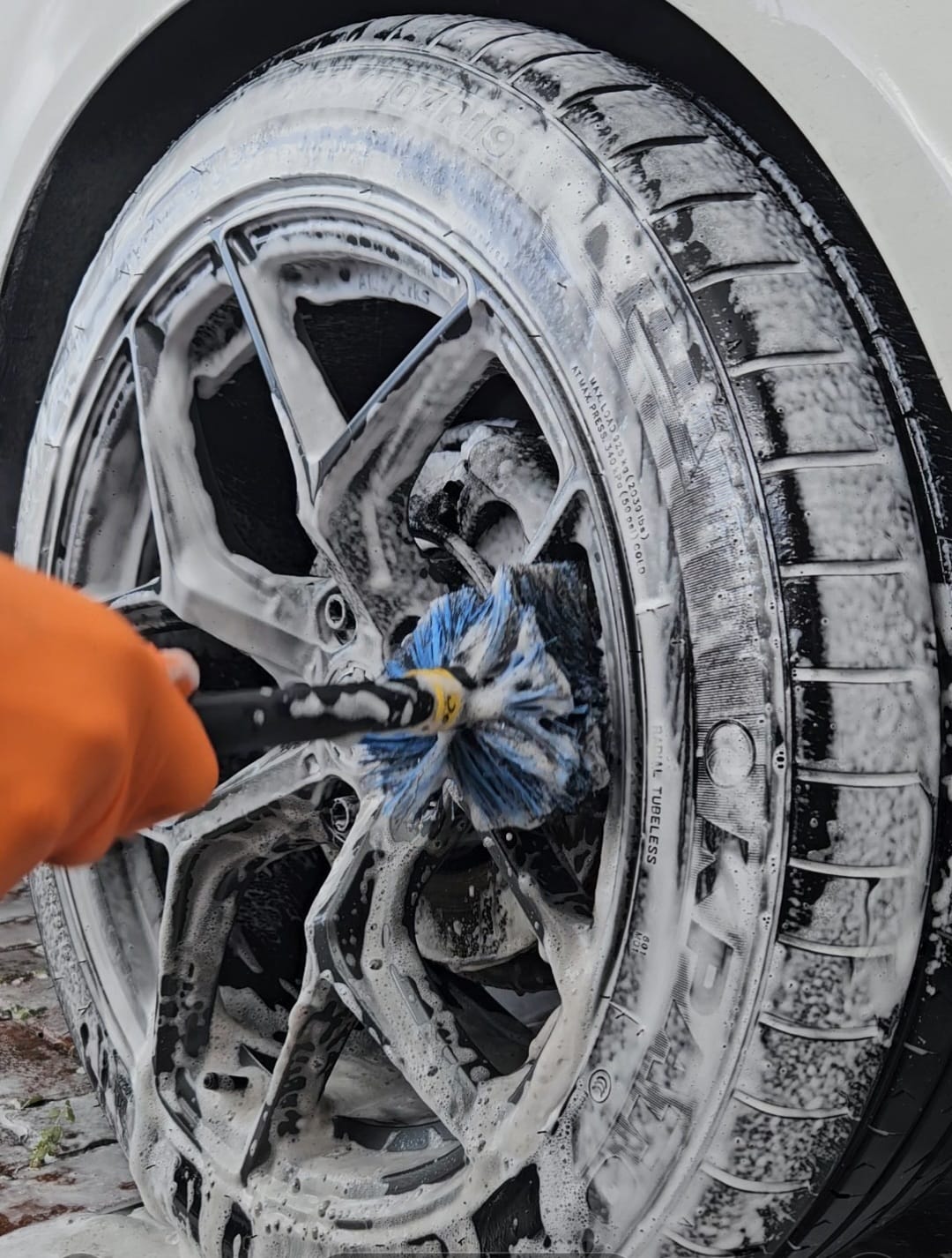 Alloy wheel covered in foam being cleaned with a detailing brush